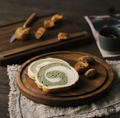Round black walnut wooden serving board with sliced bread on a linen cloth